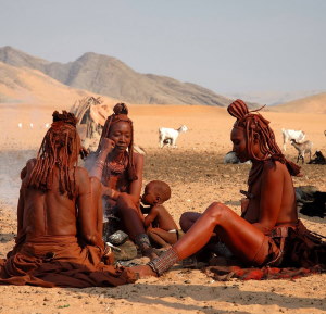 Trois jeunes femmes et un petit garçon sont assis par terre, entourés d'une nature sauvage magnifique. Ils sont en pleine conversation, partageant un moment de complicité et de découverte en plein air.