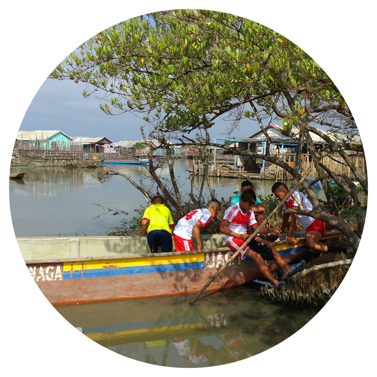 Groupe de jeunes garçons jouant sur une pirogue au bord d'un lac, entouré de maisons colorées typiques de la Colombie.