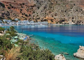 Vue d'une baie pittoresque en Crète avec des eaux turquoise cristallines et un village côtier entouré de montagnes rocheuses.