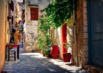 Une ruelle pittoresque en Crète, bordée de bâtiments aux murs en pierre et de pots de fleurs colorés.