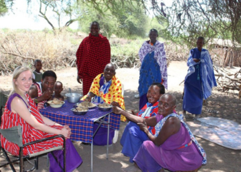 Une femme occidentale partage un repas en plein air avec un groupe de femmes et d'hommes Massaï en Tanzanie.