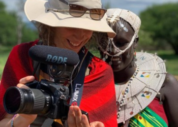 Femme occidentale filmant avec une caméra aux côtés d'une femme tanzanienne en tenue traditionnelle.