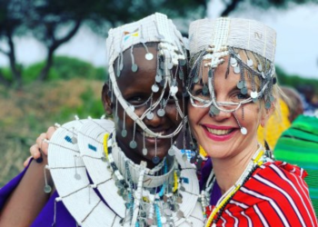 Deux femmes tanzaniennes souriantes portant des coiffes traditionnelles et des vêtements colorés lors d'une cérémonie.