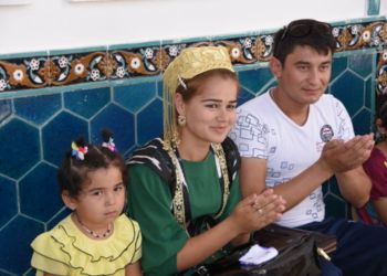 Famille ouzbèke en tenue traditionnelle, assise devant un mur décoré de carreaux bleus.