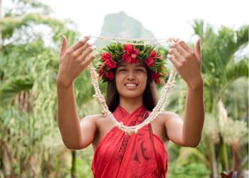 Femme polynésienne souriante en tenue traditionnelle rouge avec couronne de fleurs et collier de coquillages