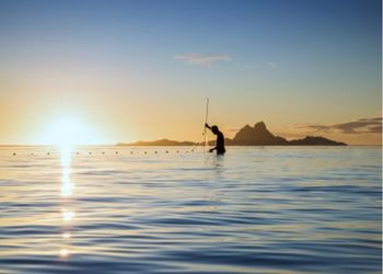 Pêcheur polynésien au coucher du soleil dans un lagon tropical