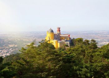 Maison jaune perchée au sommet d'un rocher couvert de forêt avec une vue panoramique sur la ville au Portugal.
