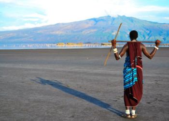 Un guerrier Maasai marchant sur une plaine en Tanzanie avec une montagne en arrière-plan