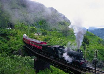 Un train en marche avec de la fumée s'échappant, traversant une ville au Sri Lanka avec une vue incroyable sur la nature et les montagnes, capturé lors d'une visite de la ville avec Odyssee des Papillons.
