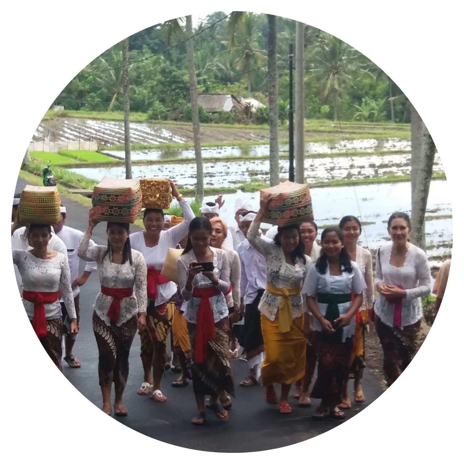 Groupe de femmes traversant un village de Bali vêtues de tenues traditionnelles, avec des rizières en toile de fond.