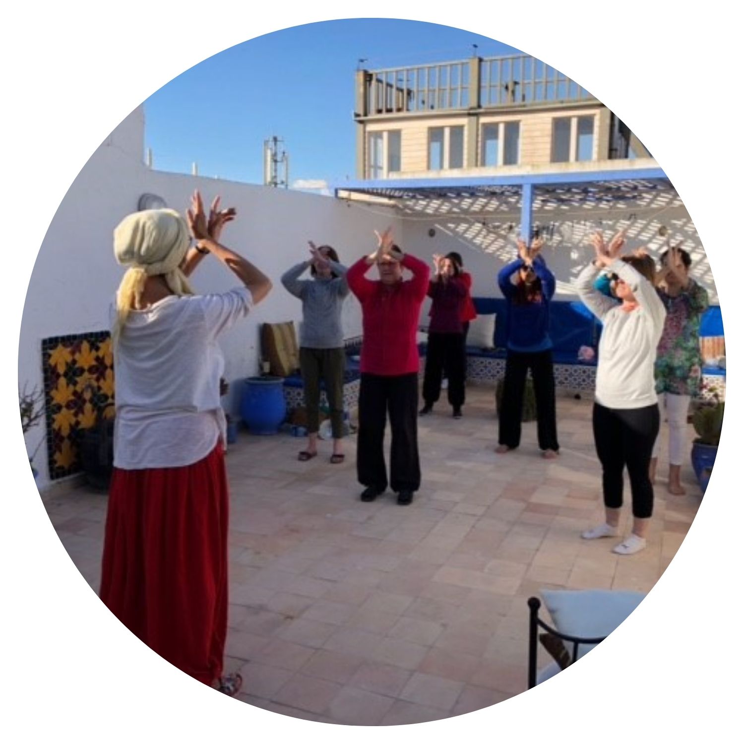 Un groupe d'environ huit femmes pratique le yoga sur une terrasse ensoleillée au Maroc. Elles sont alignées sur des tapis de yoga, exécutant différentes postures sous la direction d'une instructrice.
